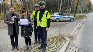 na zdjęciu dwóch umundurowanych policjantów, którzy stoją obok kobiety i mężczyzny na poboczu. W tle radiowóz policyjny.