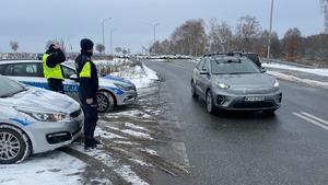 na zdjęciu umundurowani policjanci obserwujący przy drodze jadący pojazd autonomiczny