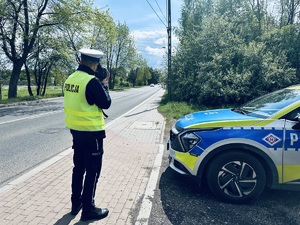 na zdjęciu umundurowany policjant ruchu drogowego, który na drodze dokonuje pomiaru prędkości