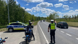 na zdjęciu oznakowany radiowóz policyjny, motocykl policyjny, dwóch policjantów ruchu drogowego, którzy zatrzymują motocyklistę do kontroli