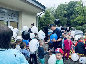 na zdjęciu umundurowany policjant rozdaje dzieciom balony