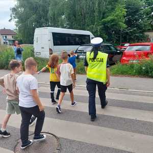 na zdjęciu umundurowana policjantka z ruchu drogowego przeprowadza dzieci przez przejście dla pieszych