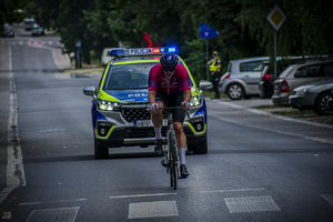 na zdjęciu rowerzysta a za nim oznakowany radiowóz policyjny