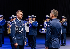 na zdjęciu dwóch umundurowanych policjantów, a w tle orkiestra