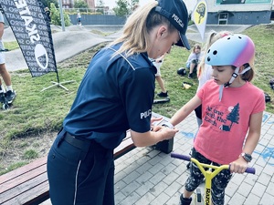 na zdjęciu umundurowana policjantka wręcza dziewczynce na hulajnodze opaskę odblaskową