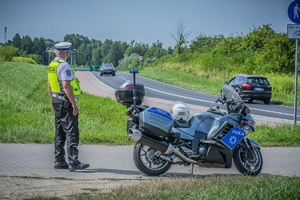 na zdjęciu umundurowany policjant stojący przy policyjnym motocyklu, który dokonuje obserwacji drogi