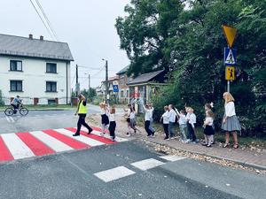 na zdjęciu umundurowany policjant przeprowadza dzieci przez przejście dla pieszych