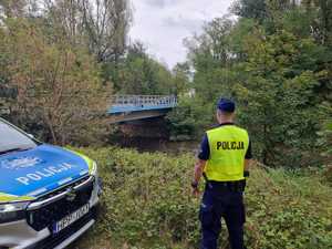 na zdjęciu umundurowany policjant stojący przy radiowozie, który monitoruje stan rzeki