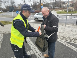 na zdjęciu umundurowany policjant wręcza starszemu mężczyźnie opaskę odblaskową