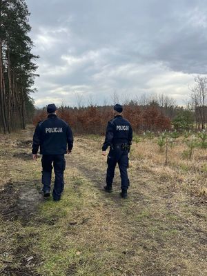 na zdjęciu dwóch umundurowanych policjantów idących ścieżką leśną