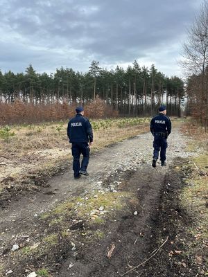 na zdjęciu dwóch umundurowanych policjantów idących ścieżką leśną