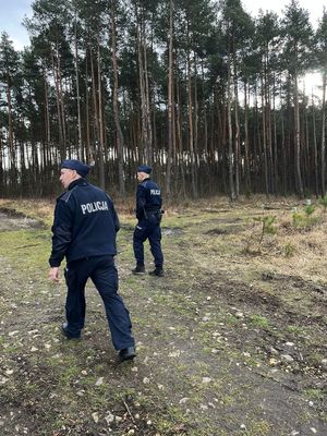 na zdjęciu dwóch umundurowanych policjantów idących ścieżką leśną