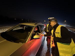 na zdjęciu umundurowany policjant wręcza kierującemu opaskę odblaskową