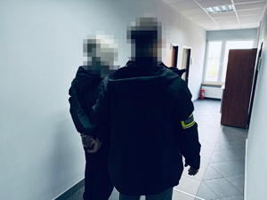 na zdjęciu nieumundurowany policjant trzyma zatrzymanego mężczyznę w kajdankach