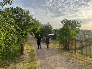 na zdjęciu dwóch umundurowanych policjantów idzie w stronę ogródków działkowych