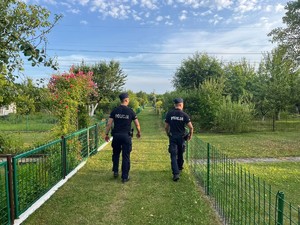 na zdjęciu dwóch umundurowanych policjantów idzie w stronę ogródków działkowych