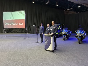 na zdjęciu komendant miejski policji przy mównicy, oraz dwóch innych umundurowanych policjantów