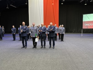 na zdjęciu umundurowani policjanci oraz przedstawiciele władz miasta składają gratulacje wyróżnionemu policjantowi