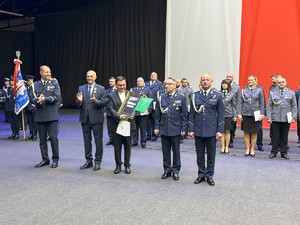 na zdjęciu kapelan policji pokazuje upominek, który otrzymał w obecności umundurowanych policjantów oraz przedstawicieli władz miasta