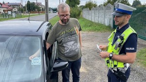 na zdjęciu policjant umundurowany wręcza kierowcy naklejkę, ktorą ten umieszcza na szybie pojazdu