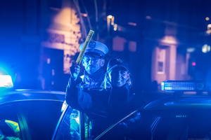na zdjęciu policjantka pokazuje do góry opaskę odblaskową a za nią stoi umundurowany policjant