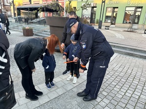 na zdjęciu umundurowany policjant wręcza dziecku opaskę odblaskową