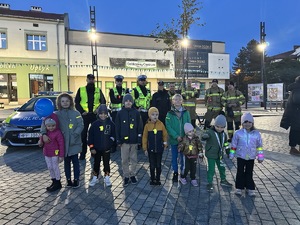 na zdjęciu policjanci, ze strażakami i strażnikami miejskimi, a przed nimi dzieci z odblaskami