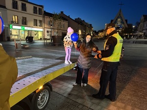 na zdjęciu umundurowany policjant daje kobiecie opaskę odblaskową