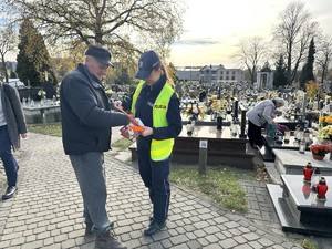na zdjęciu policjantka wręcza starszemu mężczyźnie opaskę odblaskową