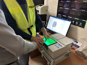 na zdjęciu technik kryminalistyki wykonuje daktyloskopię zatrzymanemu mężczyźnie