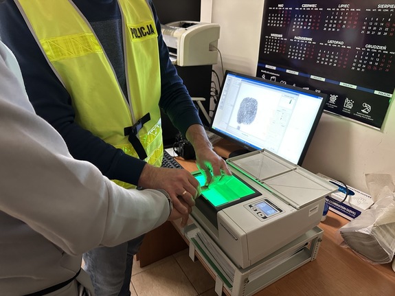 na zdjęciu technik kryminalistyki wykonuje daktyloskopię zatrzymanemu mężczyźnie