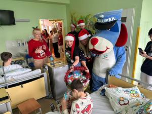 na zdjęciu kobieta częstuje dziecko słodyczami a obok stoi maskotka policji - sznupek