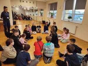 przedstawicielka sanepidu przeprowadza z dziećmi doświadczenie w tle funkcjonariusz policji