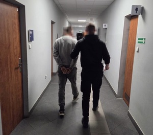 na zdjęciu nieumundurowany policjant prowadzi zatrzymanego w kajdankach