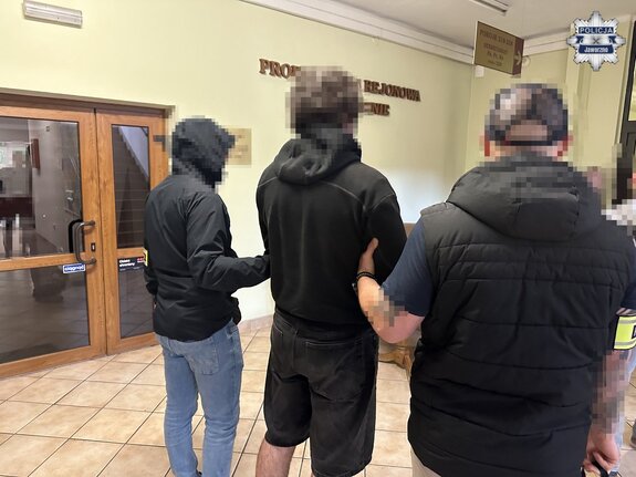 na zdjęciu dwóch nieumundurowanych policjantów trzyma zatrzymanego mężczyznę w budynku prokuratury